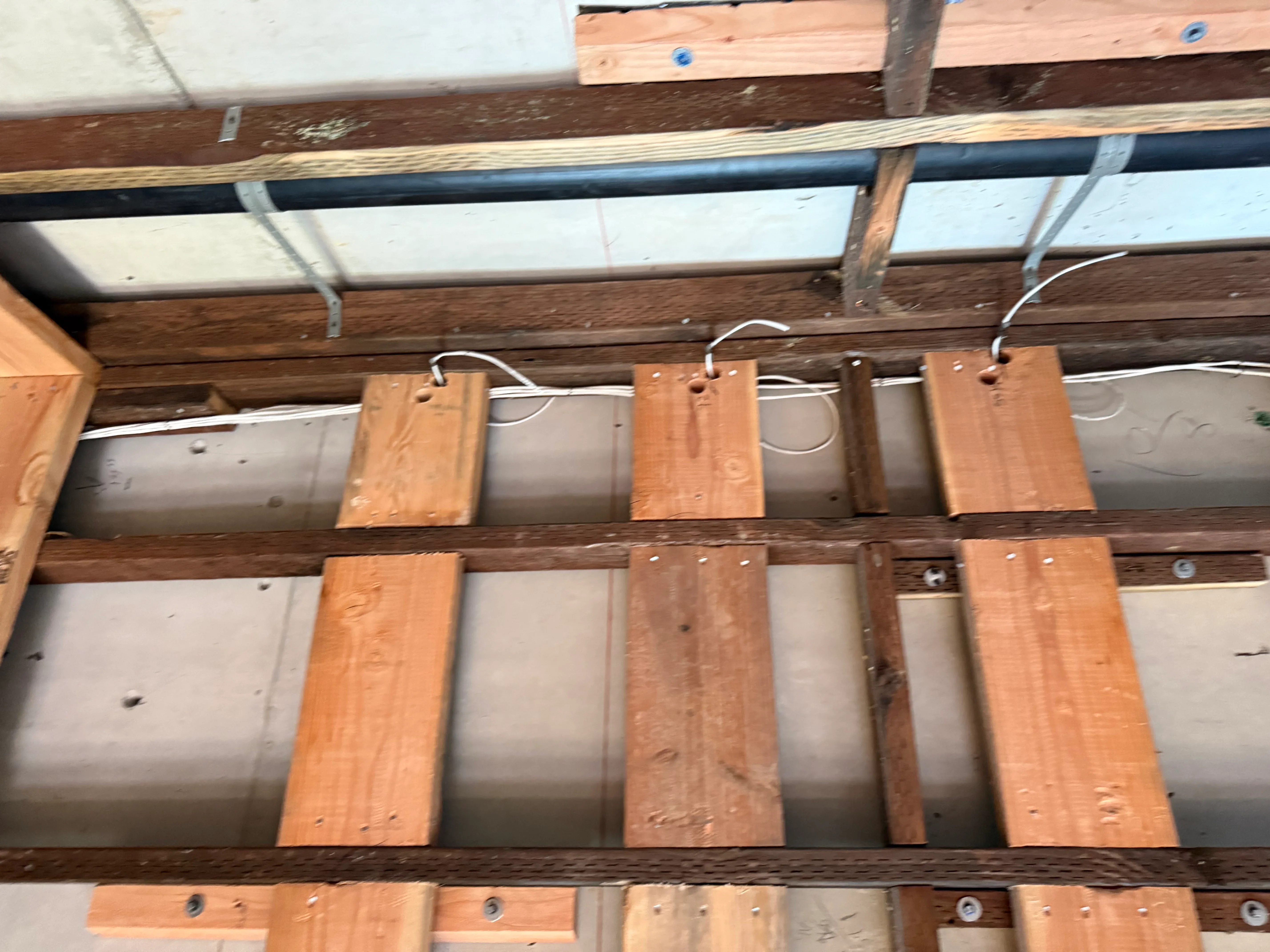 PVC conduit and Romex cable routed through wooden ceiling joists with mounted junction boxes and metal brackets