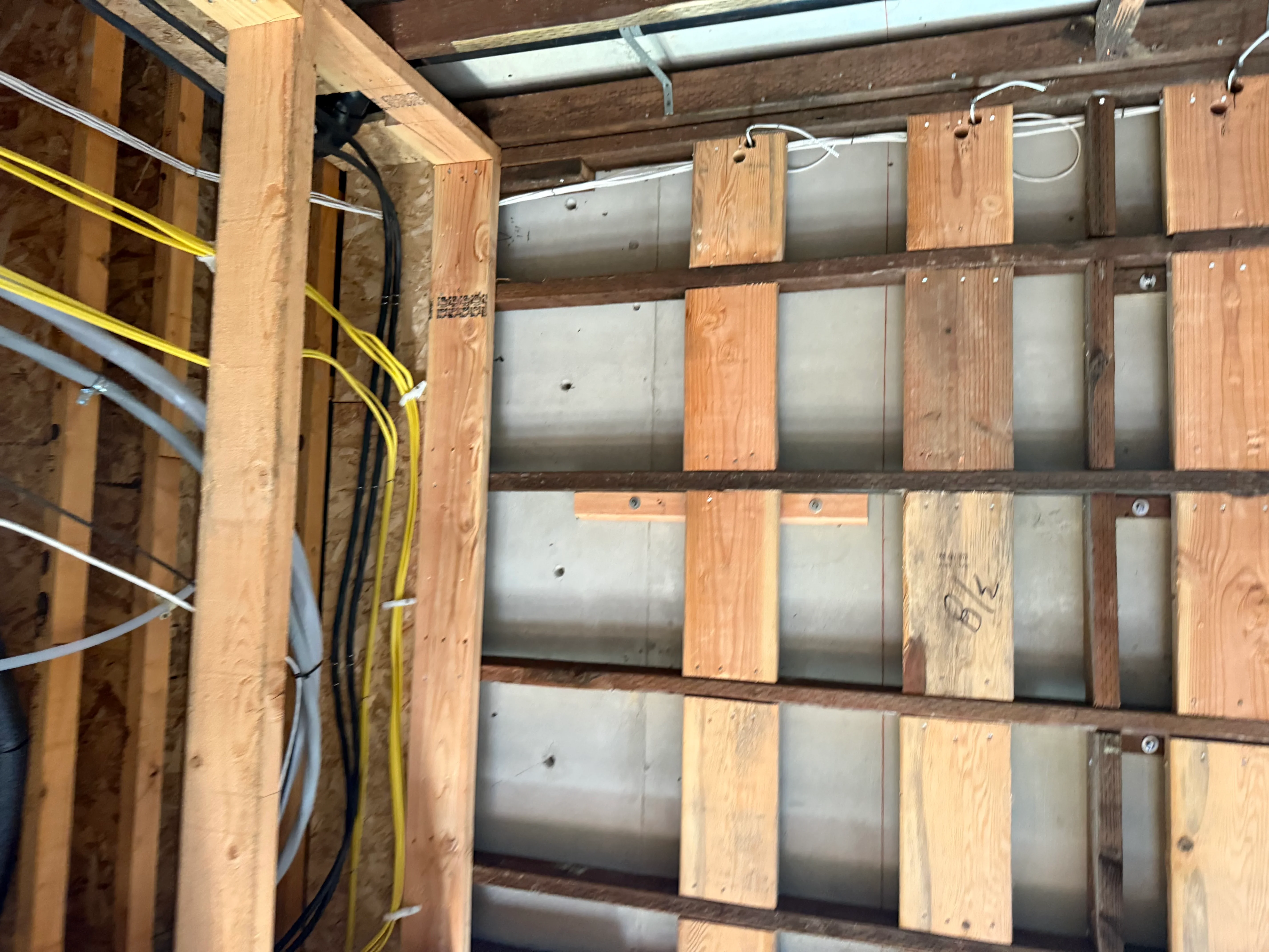 Metal electrical conduit with yellow and white wiring routed through wooden blocking and framing