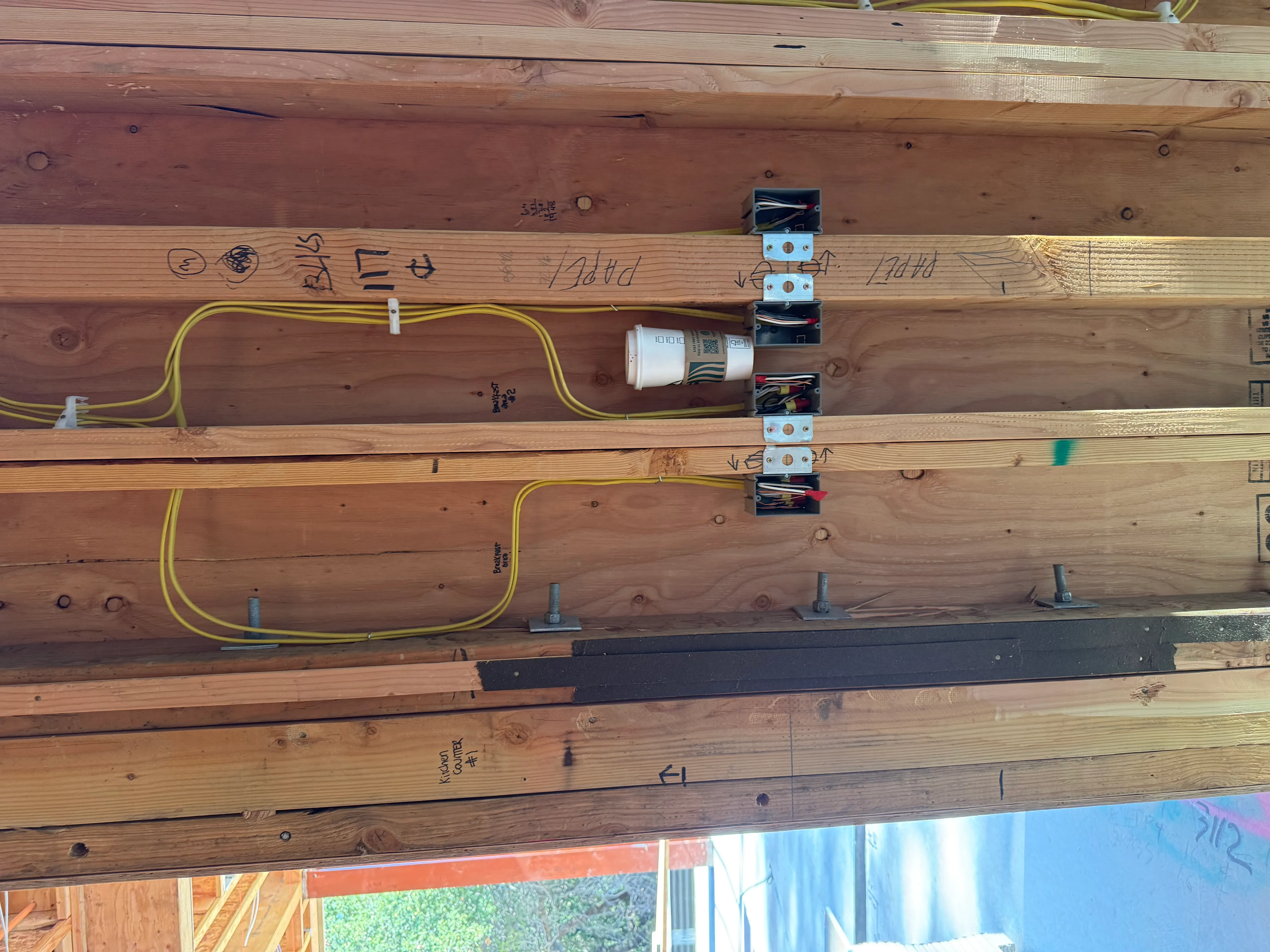 Electrical rough-in with yellow Romex cable, outlet boxes, and breaker panel on wooden beam framing